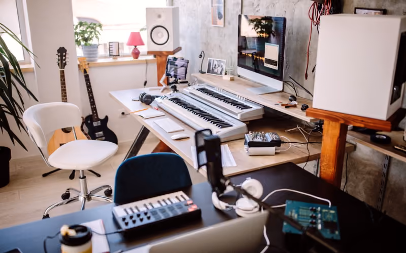 A home recording studio with a MIDI keyboard, guitars, studio monitors, and an audio interface